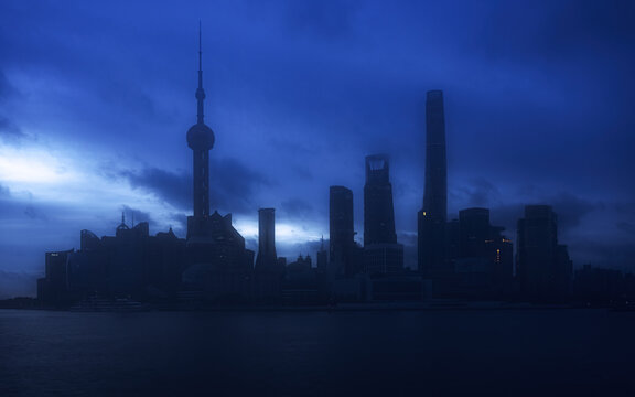 View of the Shanghai skyline at dusk featuring the Oriental Pearl Tower and Shanghai Tower silhouetted against a deep blue sky over the Huangpu River in Shanghai, Shanghai, China.
