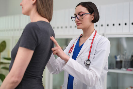 Female doctor gently checks patient back during clinical consultation in bright medical office, showing attentive care, diagnostic examination, trust, wellness support, and professional healthcare
