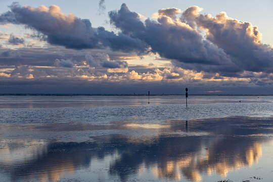 View of the calm coastal waters reflecting dramatic sunset clouds at low tide in Allingabro, Jutland, Denmark.