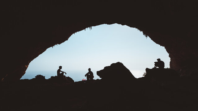 View of silhouettes of three people sitting inside the entrance of Hoq Cave looking out towards the sea in Socotra, Socotra, Yemen.