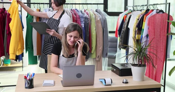 Dry-cleaning worker checks customer inquiry as boss talks on telephone. Colleague records important details about noticeable imperfections of garments