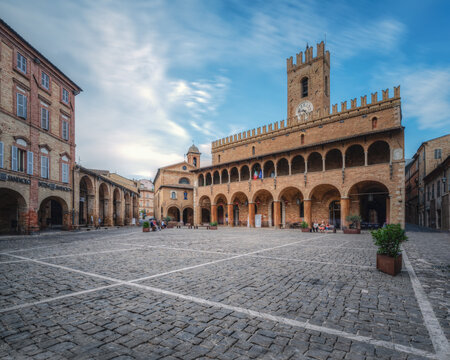 View of the historic Piazza del Popolo with its iconic brick clock tower and elegant arched porticos in the town square of Offida, Marche, Italy.