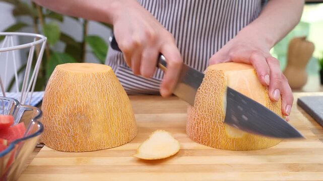 Cook in apron cuts ripe fragrant melon on wooden cutting board. Woman uses sharp stainless-steel knife to cut into evenly shaped pieces time lapse
