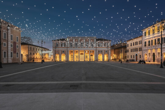 View of Piazza del Duca in Senigallia at night, illuminated by festive string lights hanging above the historic square, surrounded by elegant architecture in Senigallia, Marche, Italy.