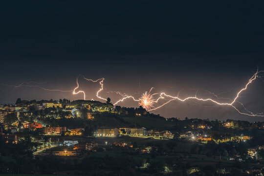 View of lightning strikes and fireworks illuminating the night sky over the historic town of Morrovalle, Marche, Italy.