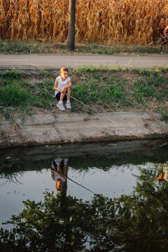 Young girl fishing by water channel reflection