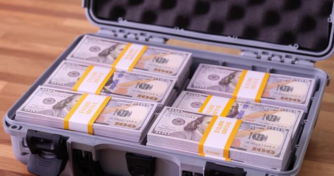 Neatly arranged bundles of American dollar bills fill briefcase. Compact calculating machine rests on closed lid of suitcase. Frame interruption