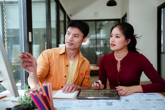 Asian designers collaborating on a creative project at a modern studio, discussing ideas and working together on design plans.