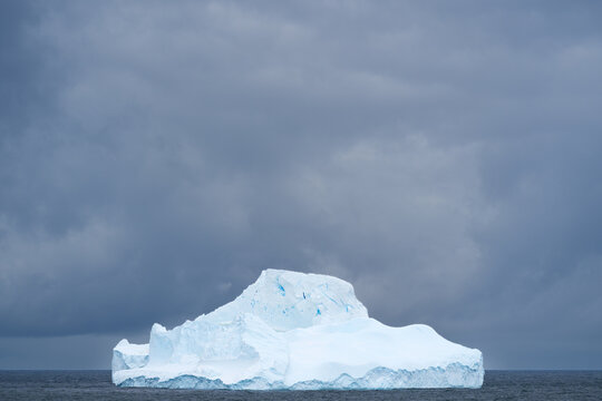 View of an iceberg floating in the ocean under a dark, cloudy sky in the South Orkney Islands.