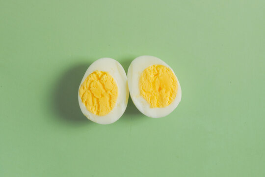 Two halves of a hard boiled egg with bright yellow yolk presented on a minimal pastel green background with generous copy space.
