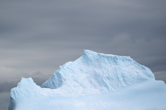 View of a large, jagged iceberg with blue-tinted ice against a dramatic, overcast grey sky in the South Orkney Islands.