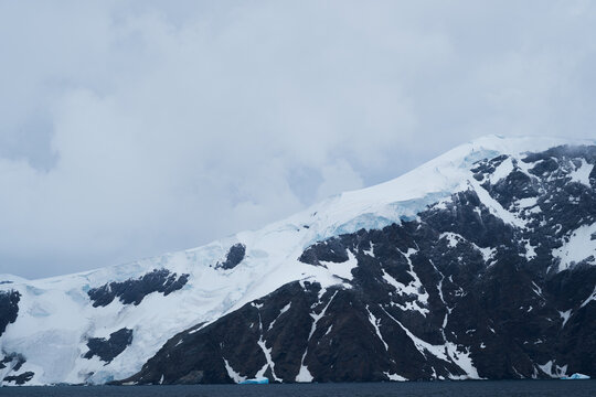 View of the snow-covered mountains and glaciers with dark rocky slopes and a cloudy sky above the sea in the South Orkney Islands.