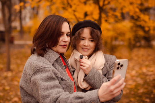 Two women female bloggers filming video blog and holding lavalier microphone during autumn walk