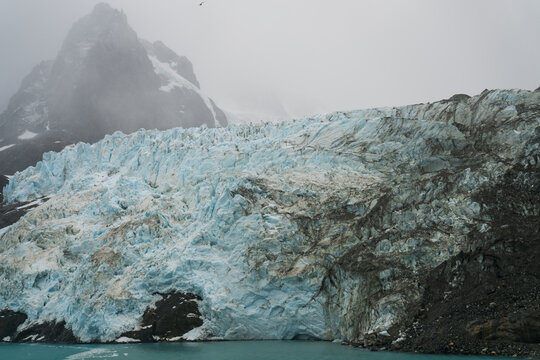 View of Drygalski Fjord glacier with its striking blue ice, rugged snow-capped mountains, and misty atmosphere in South Georgia and the South Sandwich Islands.