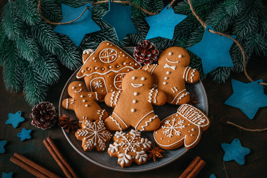 A set of Christmas gingerbread cookies on a plate against a dark rustic background with Christmas decorations, top‑down view, selective focus.