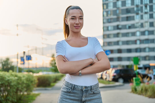 Confident young woman standing with arms crossed on city street outdoors