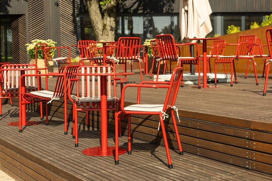 Empty outdoor cafe terrace with red metal chairs and tables in bright daylight