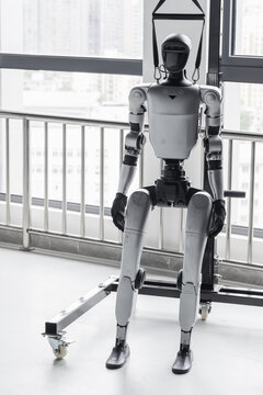 Humanoid test robot secured in a harness inside a research lab, staged for safety and mobility testing against an urban window backdrop. Industrial prototype evokes technology and experimentation
