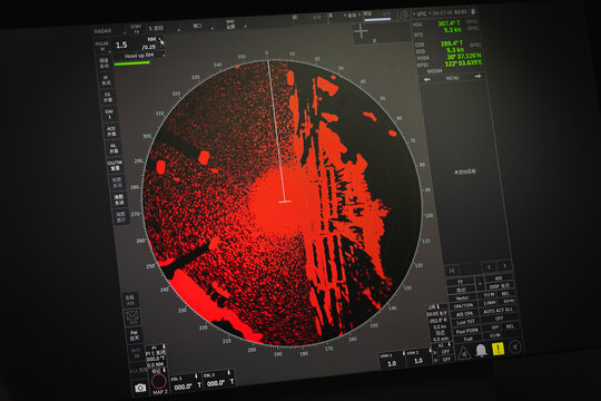Maritime radar screen on a ship bridge displaying dense red echoes, range rings and a heading marker for navigation and collision avoidance. High-contrast electronic display used for vessel tracking