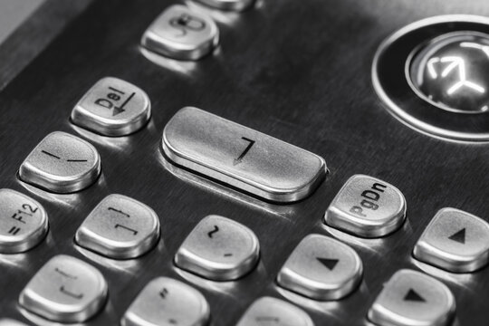 Macro view of metallic keypad buttons on a stainless steel control panel, showing worn number and arrow keys, texture and reflections that convey durability, technology and industrial design