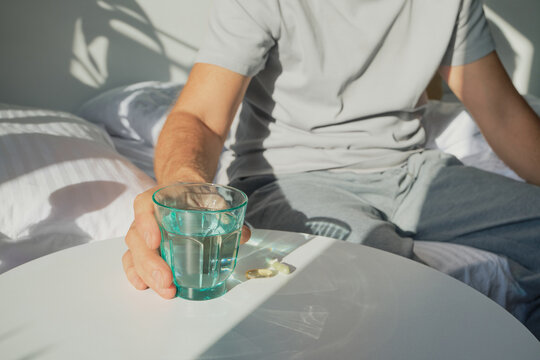 Man reaching for glass of water and vitamins on bedside table in morning