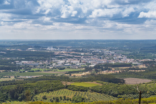 View of the town nestled among green hills and wind turbines from the Parque Eolico da Serra dos Candeeiros under a cloudy sky in Rio Maior, Santarem, Portugal.