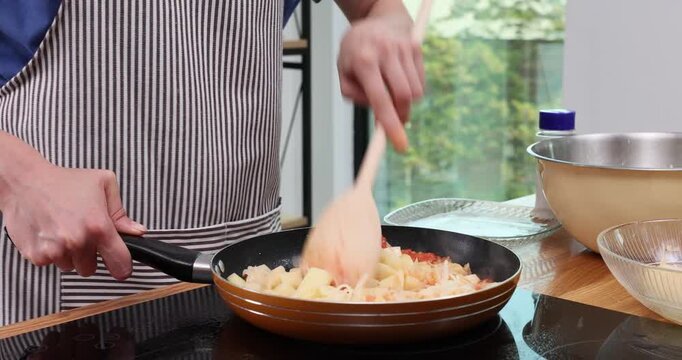 Woman chef pours potato with bacon onto hot frying pan with tomato paste in kitchen. Female cooks nutritious dinner with organic ingredients timelapse
