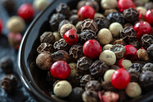 Close-up of mixed peppercorns in a black bowl on a textured surface.