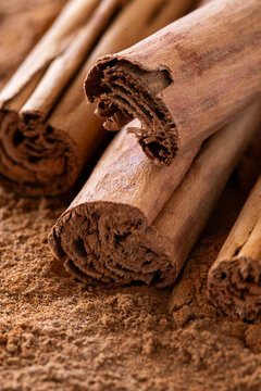 Close-up of cinnamon sticks on ground cinnamon powder in warm lighting.