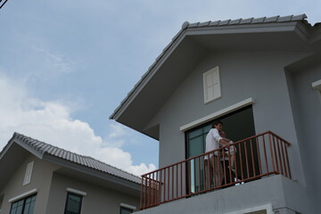 Obraz premium Caucasian family of three embracing stand at the wooden railing admiring the neighborhood view on the balcony of their new house overlooking the residential estate with copy space