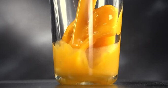 Orange juice pouring into glass in slow motion on black background