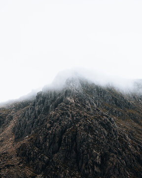 View of Tryfan mountain peak shrouded in thick mist and clouds with rugged rocky terrain in Bangor, Wales, United Kingdom.