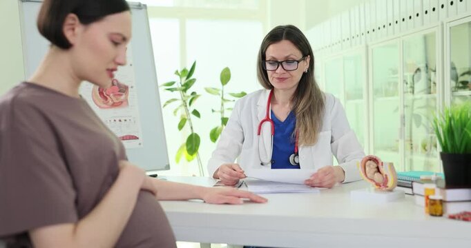 Pensive pregnant woman shares concerns with supportive gynecologist in clinic slow motion. Doctor calms down worried expecting lady at appointment