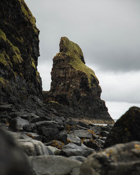 View of the rugged sea stack at Talisker Bay with dark volcanic rocks and mossy cliffs under an overcast sky in Talisker, Scotland, United Kingdom.