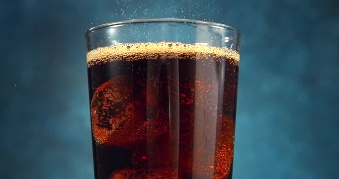 Cola bubbles bursting and spraying from a fresh fizzy drink with ice in slow motion