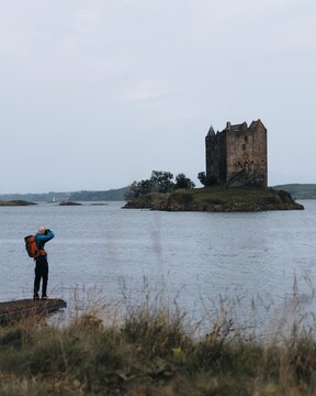 View of a photographer capturing the historic Castle Stalker on a small island in the water under an overcast sky in Appin, Scotland, United Kingdom.