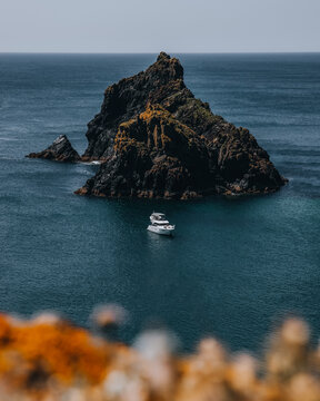View of the craggy rock formation at Kynance Cove with a small motorboat floating on the deep blue sea in Helston, England, United Kingdom.