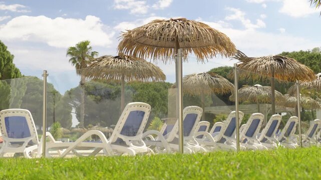 Thatched parasols shade rows of white and blue loungers beside a fenced outdoor resort pool