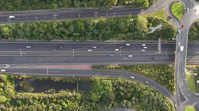 Top-down drone shot showcasing the road infrastructure of Mount Roskill, Auckland, with multiple highway lanes, turning paths, vehicles and green spaces in golden-hour light.