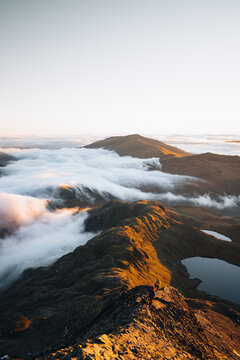 View of hikers traversing the Crib Goch ridge above a sea of clouds during golden hour in Caernarfon, Wales, United Kingdom.