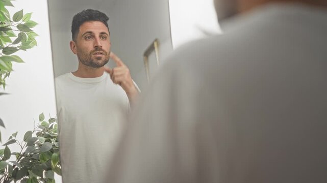 Man points to chest with hand in mirror inside a building, fist near chest as he studies his reflection; self reflection introspection.