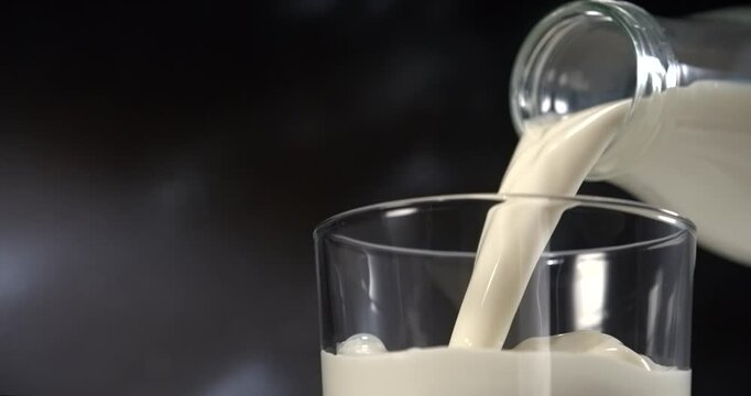 Milk pouring into glass with splash in slow motion close up black background