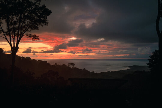 View of a dramatic sunset over the Pacific Ocean with silhouetted tropical trees and dark clouds in Uvita, Puntarenas Province, Costa Rica.