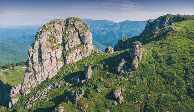 Green alpine meadow with dramatic limestone rock formation Babin Zub rising above layered mountain valleys at summer sunrise. Scenic nature background - Stara Planina park in Serbia, Balkans.