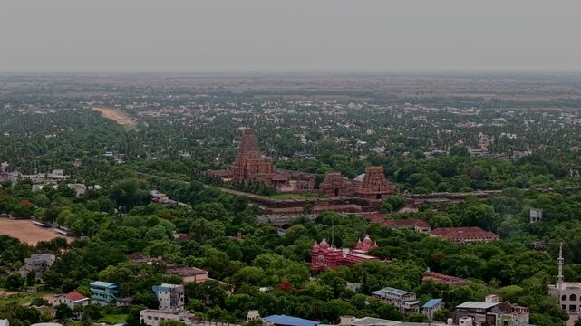 Aerial drone view prominently shows Brihadeeswara Temple rising above lush greenery with ancient towers and surrounding buildings across Tanjavur city in Tamil Nadu India