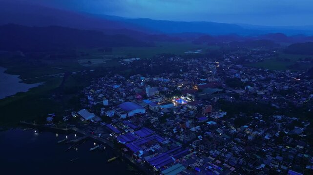 Aerial view of an illuminated basketball court during a local community event in Buhi, Camarines Sur, Philippines. Viewed from a distance during blue hour, the brightly lit court stands out as a glowi