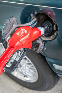 View of a red fuel nozzle inserted into a car's fuel tank filler neck at a gas station in Portland, Oregon, United States.