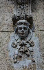 Weathered stone mascaron carved as a face on a facade corbel © Mariia