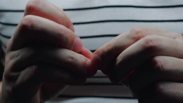 The man is nervous and is fidgeting with his fingers.
The man is picking at his fingers.