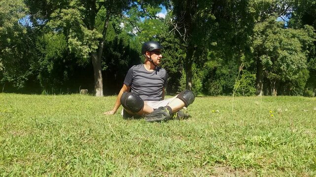 Man sitting on green grass in public park resting after inline roller skating 